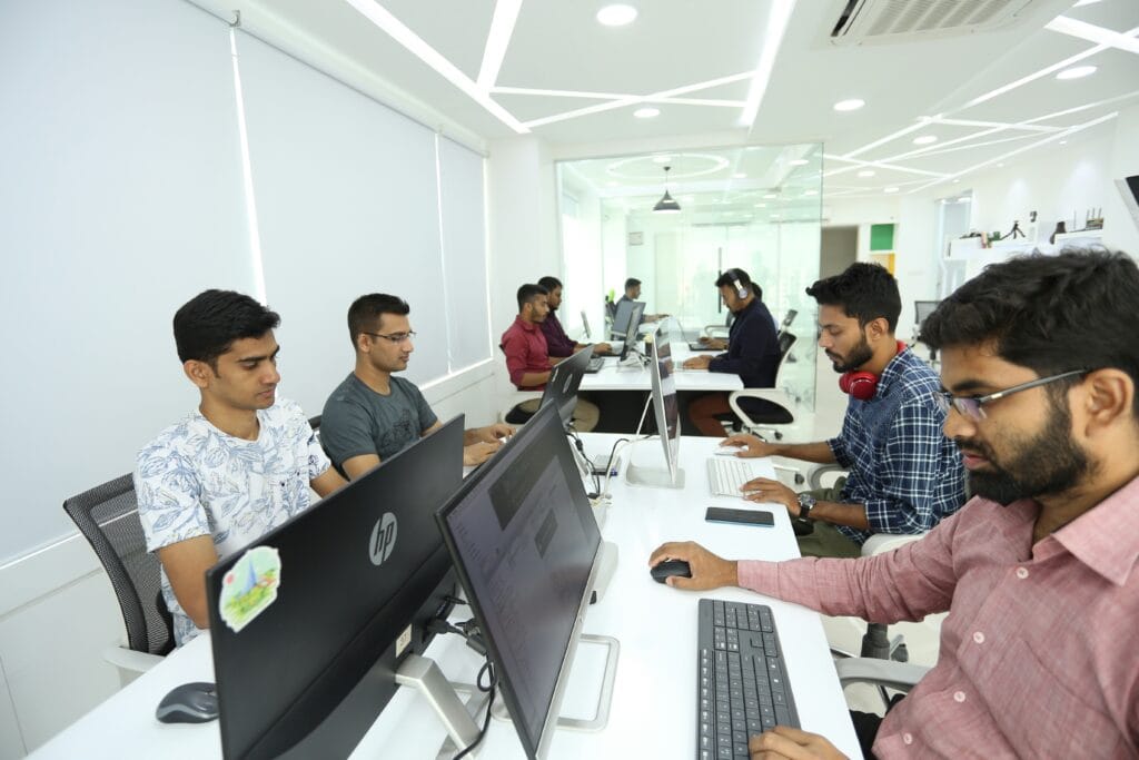 Group of young professionals working on laptops around a conference table in a modern office meeting room.
