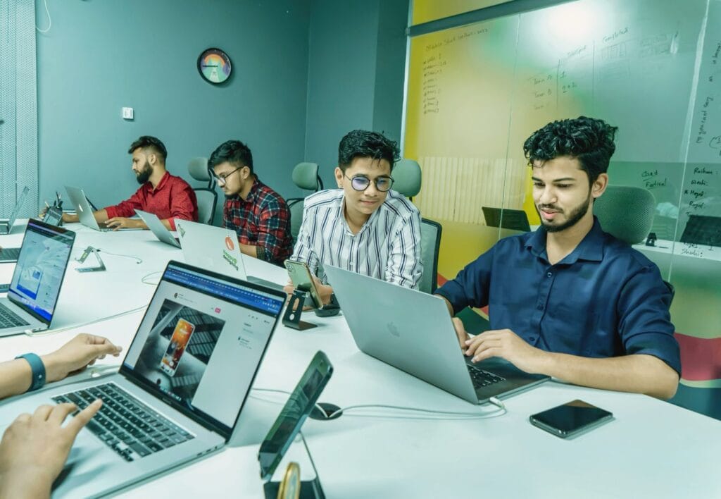 Group of young professionals working on laptops around a conference table in a modern office meeting room.