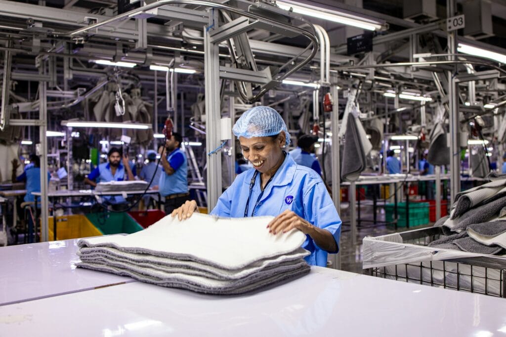 Worker in a blue uniform and hairnet folding stacked fabric at a textile factory production line.
